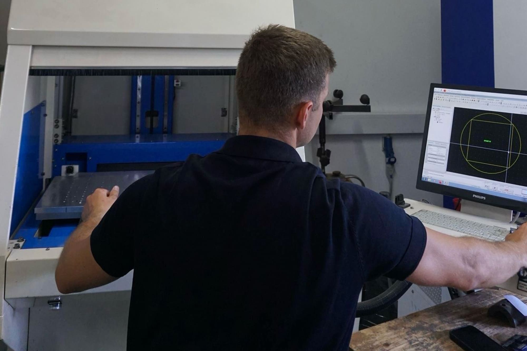 Mann in einem Poloshirt bedient ein Lasergerät mit angeschlossenem Monitor, der technische Daten anzeigt